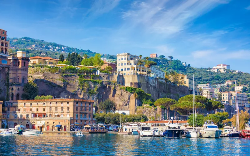 Harbor View of a Mediterranean Town with Boats Docked Along a Rocky Waterfront and Hillside Homes.