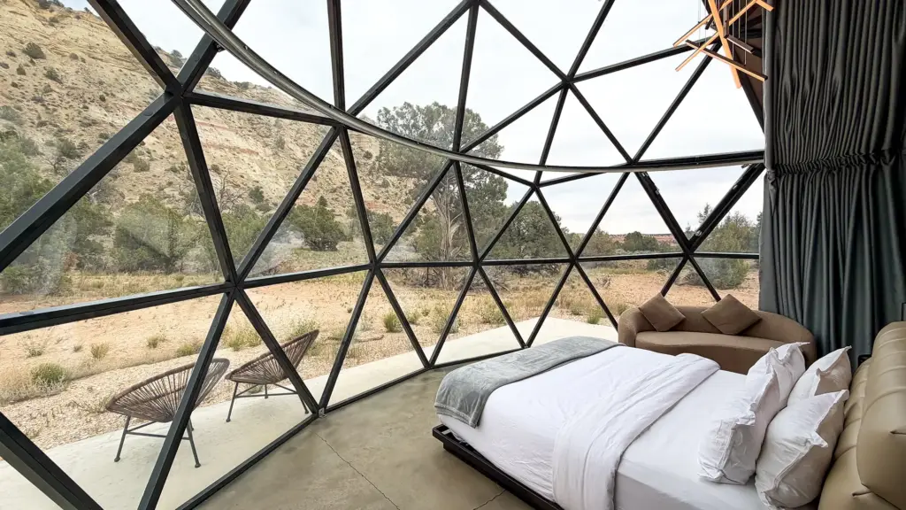 Geodesic Glass-dome Bedroom with Two White Beds and Desert Landscape Outside the Panels.
