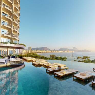 High-rise Hotel with Multiple Balconies Beside an Infinity Pool and a Row of White Loungers Facing the Sea.