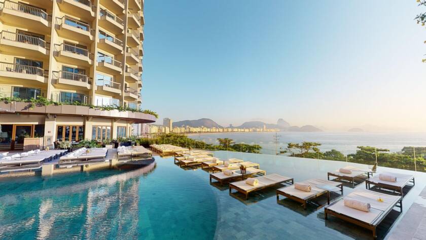 High-rise Hotel with Multiple Balconies Beside an Infinity Pool and a Row of White Loungers Facing the Sea.