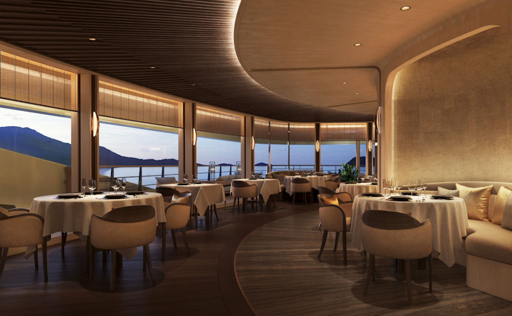 Amangati aman grill 03 1890x1167px | The Luxury Travel Atlas | The Luxury Travel Atlas Elegant Restaurant Interior with Round Tables Set for Dining, Beige Chairs, and Warm Lighting, Overlooking a Sunset Seascape Through Large Windows.