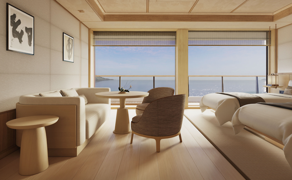 Hotel suite living area with beige sofa, round table, two chairs, and a bed, large window revealing the ocean.