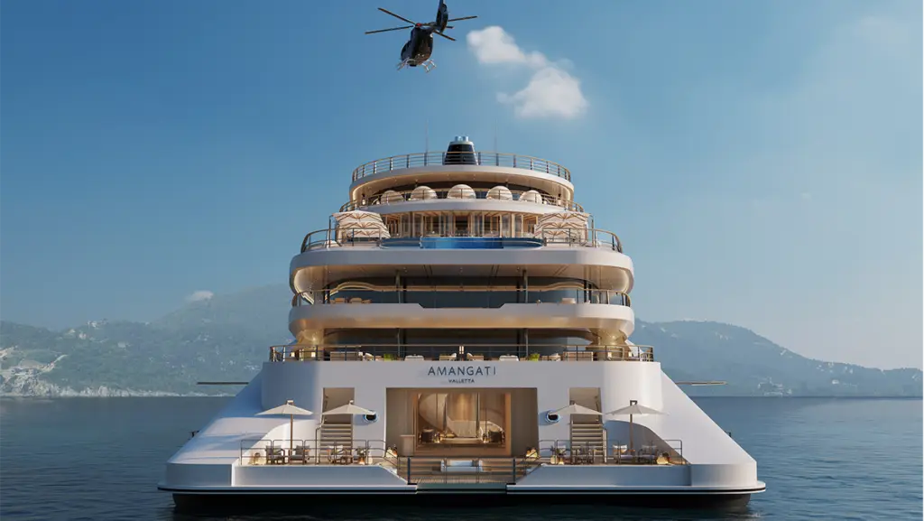 Front view of a white multi-deck luxury yacht named AMANGATI VALLETTA on calm sea, with a helicopter hovering overhead.