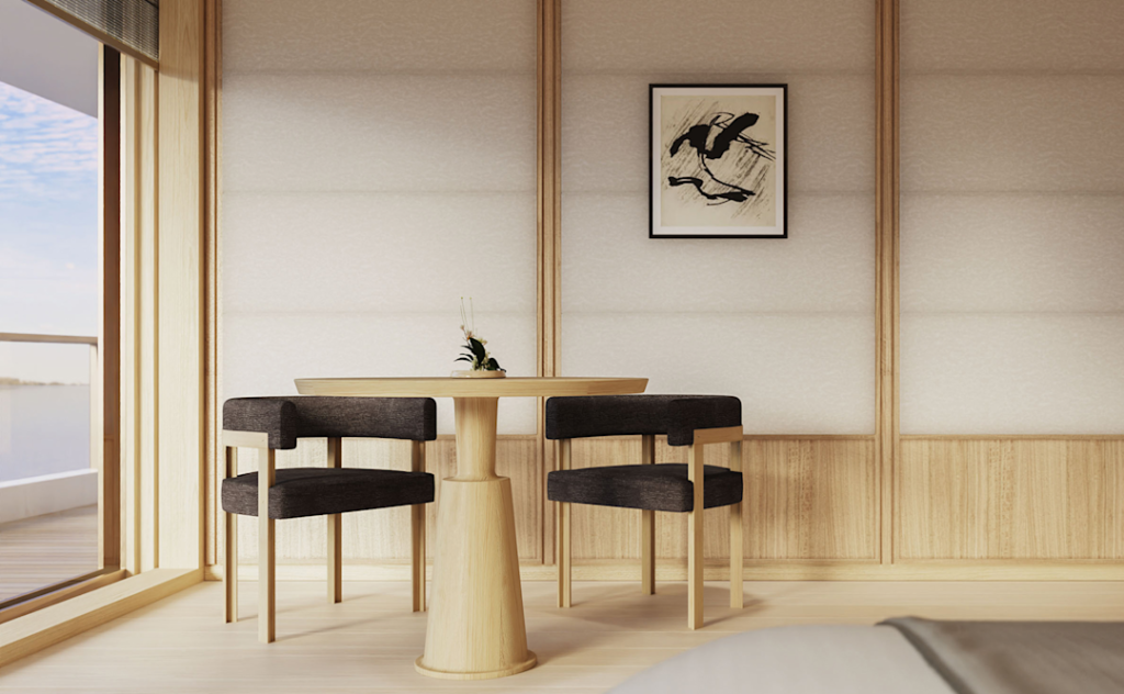 Minimalist dining nook with a round wooden table and four grey upholstered chairs in a sunlit, wood-paneled room overlooking water outside the window.