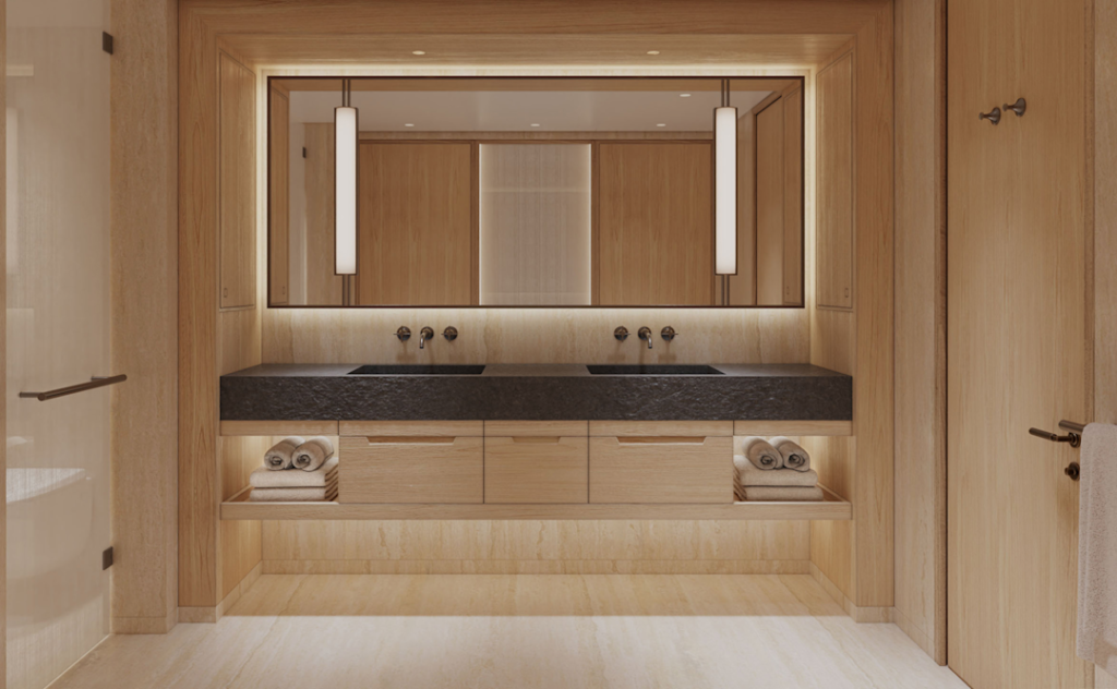 Wood-clad bathroom vanity with a dark countertop and dual sinks, large mirror, and built-in towel shelves with rolled towels under warm lighting.