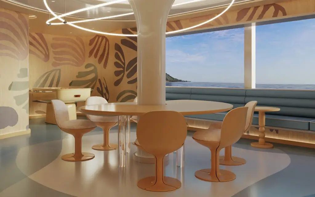 Amangati youth lounge 01 1394x1394px | The Luxury Travel Atlas | The Luxury Travel Atlas Circular Table with Peach Chairs in a Bright Seaside Dining Area, Large Windows Showing the Ocean and Blue Sky.
