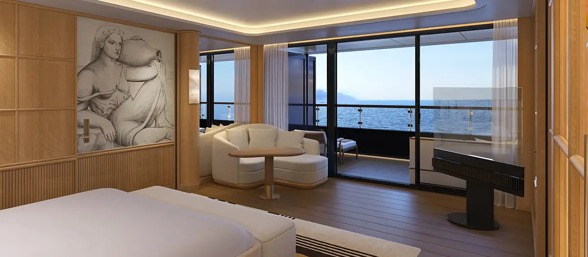 Luxurious hotel suite with a white bed, white seating area, and a balcony overlooking the sea through floor-to-ceiling glass doors.