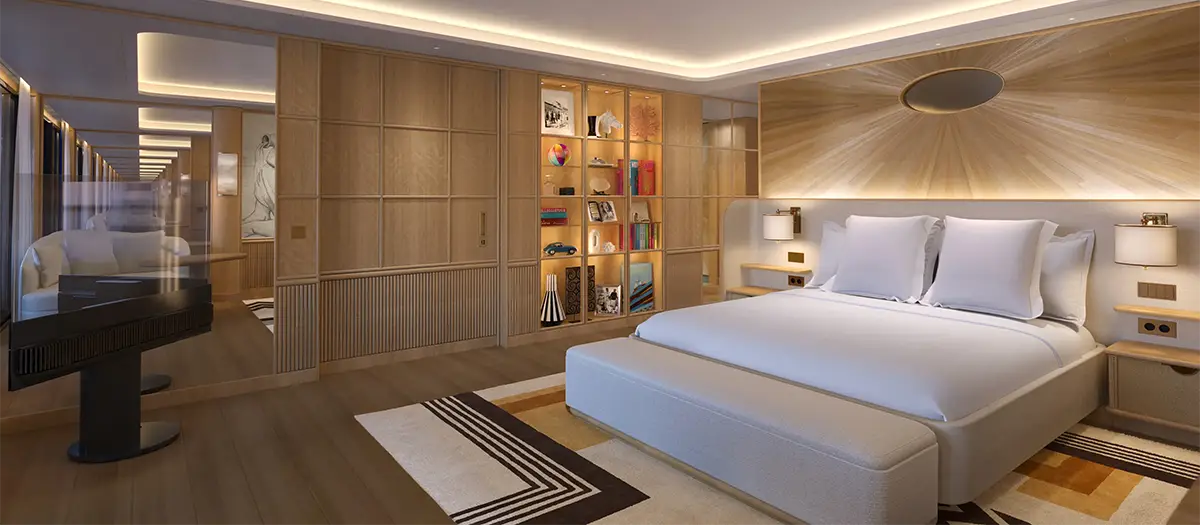 Modern hotel room with a large white bed, padded headboard, and built-in shelving displaying books and decor on the left side.
