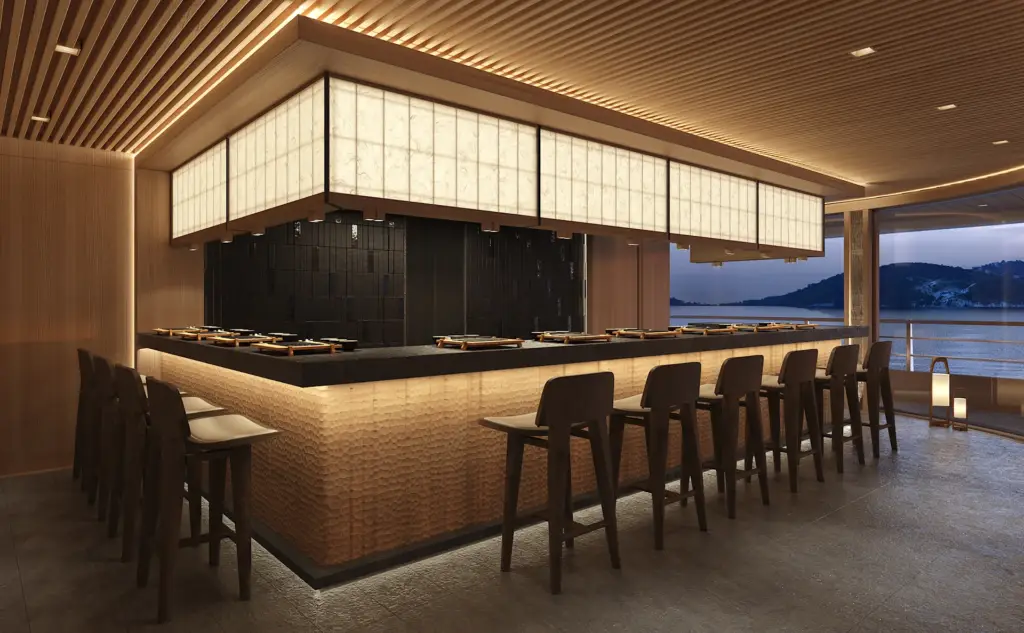 Hiori hero image | The Luxury Travel Atlas | The Luxury Travel Atlas Luxurious Sushi Bar with a Long Granite Counter, Dark Tiled Back Wall, and Warm Wooden Decor Overlooking Water Through Large Windows.