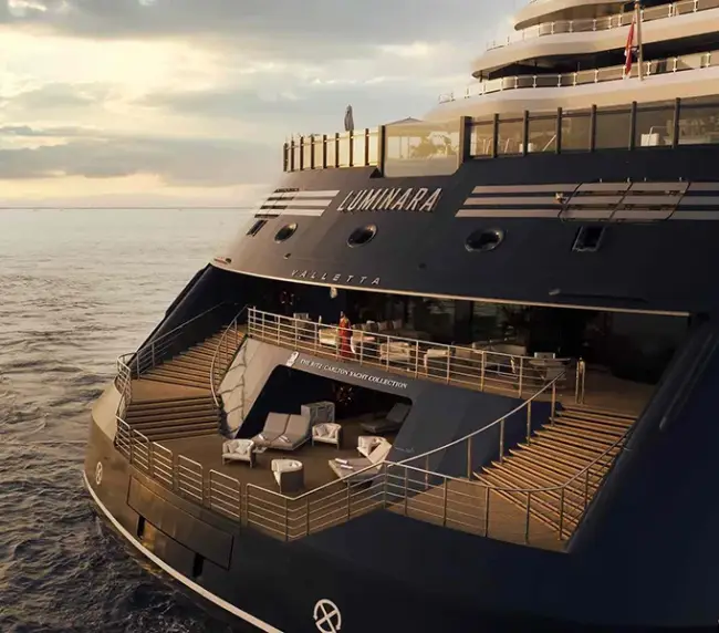 Rear Deck of a Luxury Yacht Named Luminara with White Lounge Seating, Glass Railings, and Sunset over Calm Sea, Stern Area Visible.