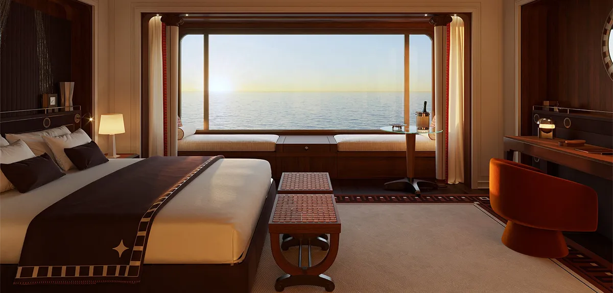 Luxurious hotel cabin with a large bed, dark brown linens, and a window seating area overlooking the ocean at sunset/ocean view.