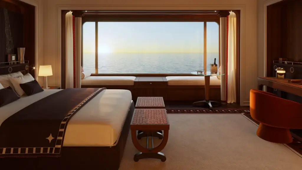 Luxurious ocean-view cruise cabin with a large bed, seating area by the window, and warm ambient lighting as the sun sets over the sea.