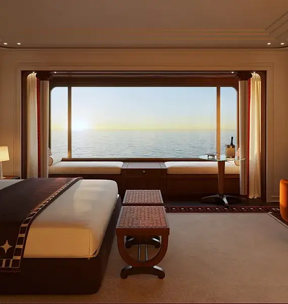Orient Express Yachts Feature 02 | The Luxury Travel Atlas Luxurious Hotel Bedroom with a King Bed, Warm Lighting, and an Ocean-view Window.
