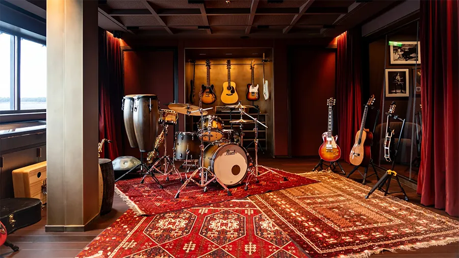 Orient Express sailingyachts corinthian le salon de musique | The Luxury Travel Atlas | The Luxury Travel Atlas Professional Music Studio with a Pearl Drum Kit on a Red Patterned Rug, Surrounded by Guitars on Stands and Wall-mounted Guitars in Warm Lighting.”,