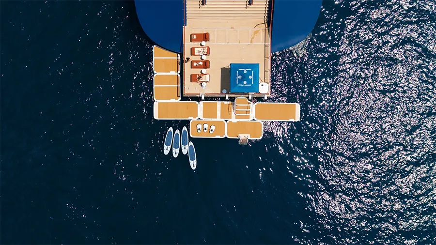 Orient express corinthians la Marina | The Luxury Travel Atlas | The Luxury Travel Atlas Aerial View of a Boat's Rear Deck with Tan Lounge Chairs, Paddle Boards, and a Small Blue Safety Box, Surrounded by Dark Blue Water.