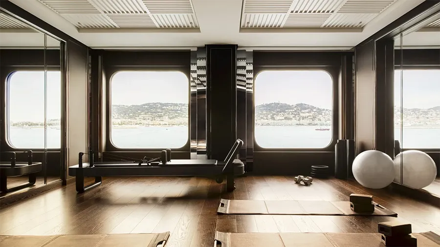 Orientexpress sailingyachts corinthian le Gymnase | The Luxury Travel Atlas | The Luxury Travel Atlas Sunlit Fitness Studio with Large Windows Overlooking Water; Pilates Reformer, Mats, Stability Balls, and Blocks on a Wooden Floor.