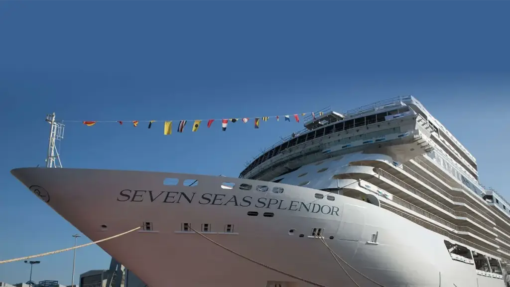Front view of a large white cruise ship named Seven Seas Splendor docked at port with colorful signal flags overhead.