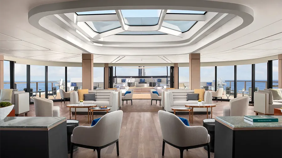Luxurious Ocean-view Lounge with White Sofas, Wooden Floors, and a Central Skylight Letting in Natural Light, Overlooking the Sea on a Cruise Ship.