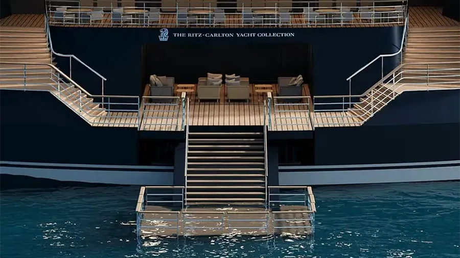Luxurious Yacht Deck with Beige Sofas, Glass Tables, and a Central Staircase Down to a Floating Platform on Calm Blue Water, the Ritz-carlton Yacht Collection Sign Visible Above the Seating Area.