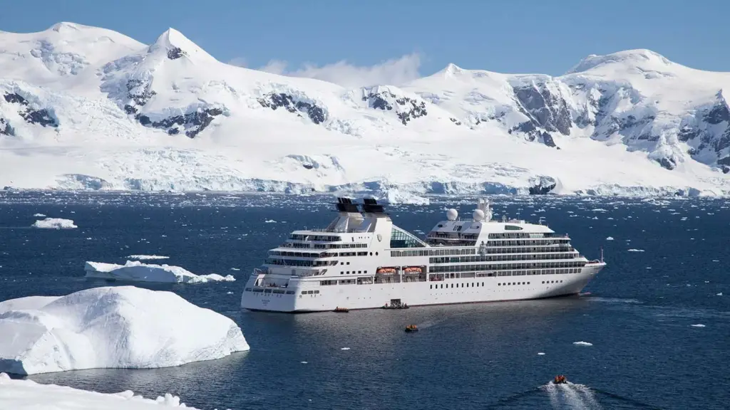 Large white cruise ship sailing through deep blue polar waters with snow-covered mountains in the background