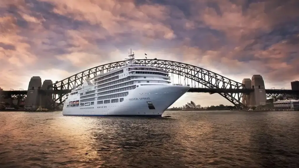 White cruise ship named Silver Spirit sailing under the Sydney Harbour Bridge at sunset.