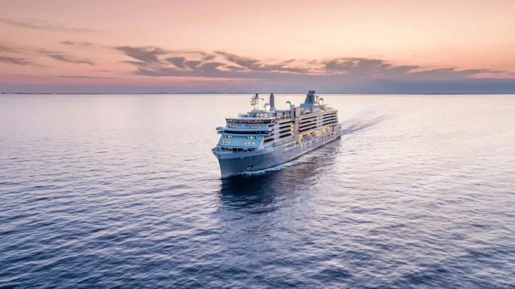 Cruise ship sailing on calm ocean at sunset with pink-orange sky behind it