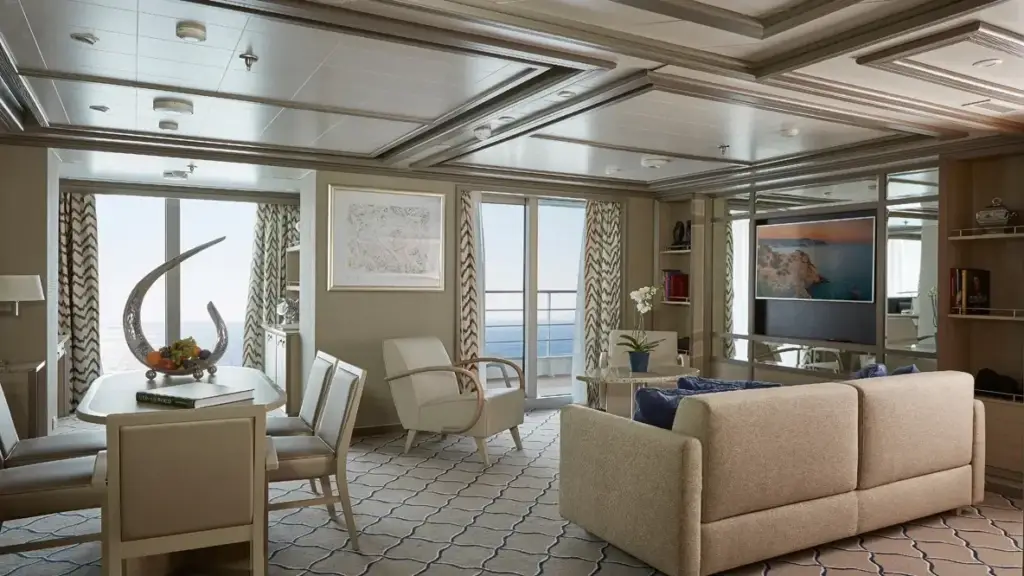 Luxurious living and dining area with beige sofa, white chairs, and a glass table facing a sea-view balcony.